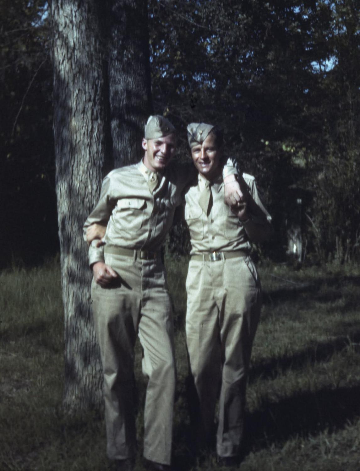 Two cadets in khaki shirts and garrison caps, arms around each other under pine trees at Maxwell Field, 1943: Red Carpenter at left, Frank Calicura at right