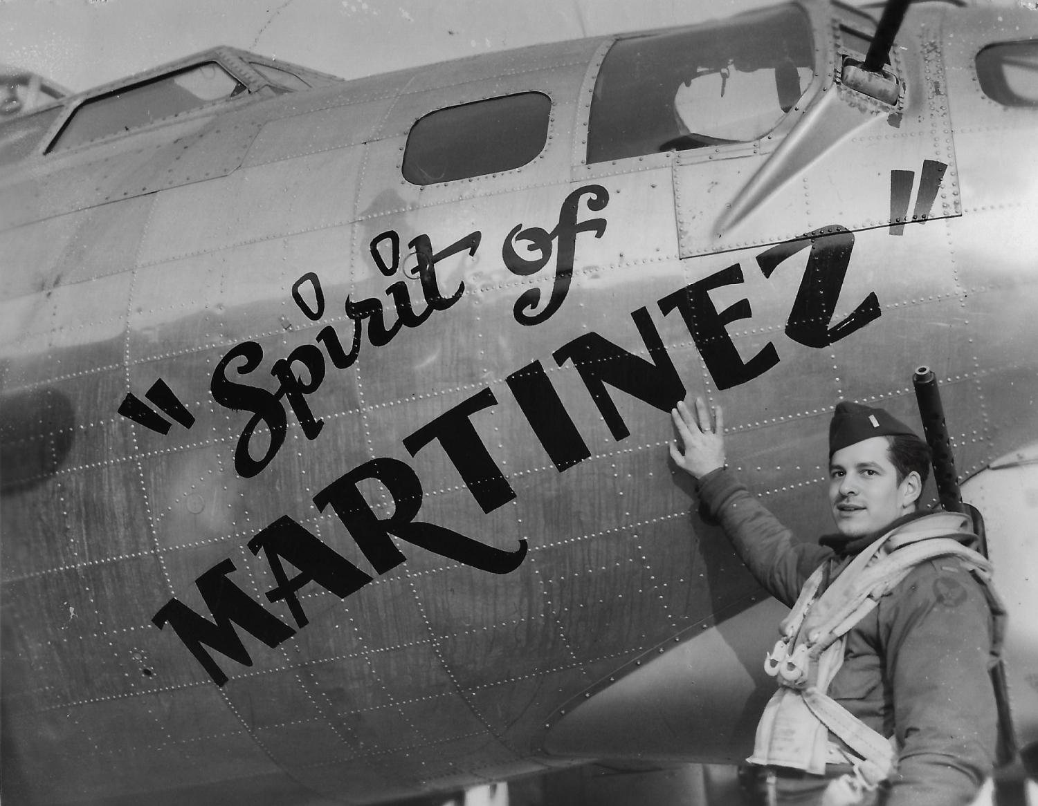 Frank Calicura in flying kit standing at the painted nose of a B-17, his hand on the word MARTINEZ