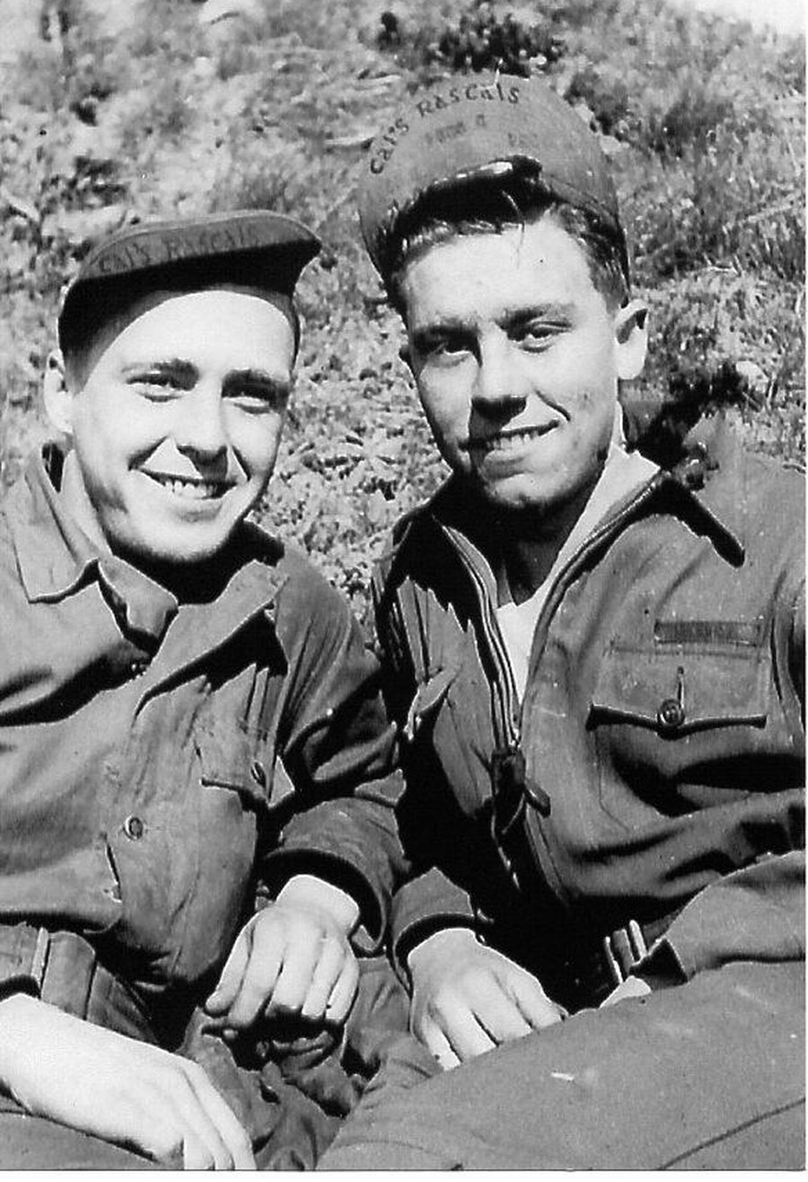 Robert E. Collins and Marvin L. Markus sitting on a hillside in flying jackets, both wearing ball caps